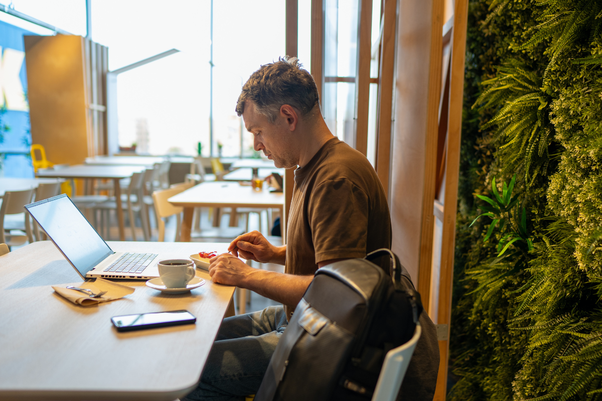 A man sitting a table working on a laptop with a coffee..